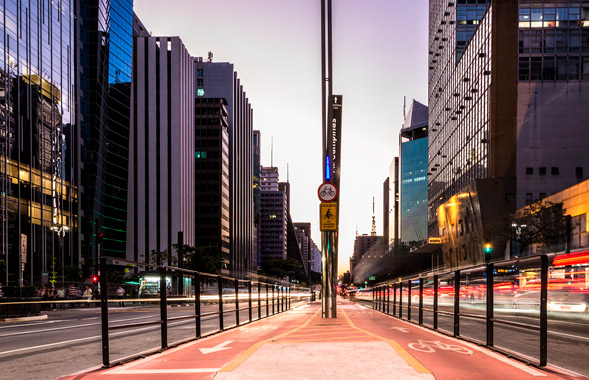 Visão do meio de uma ciclovia no meio de duas pistas de carros no anoitecer em uma cidade grande.